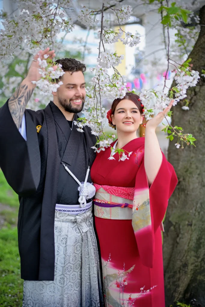 Couple in traditional kimono and hakama at Sumida River, Asakusa Tokyo — cherry blossom tree in foreground