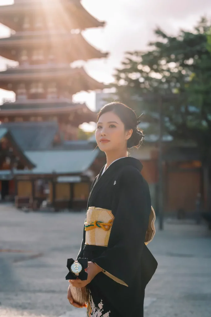 Guest in a black kimono with gold obi backlit by low evening sun, the five-story pagoda blurred behind