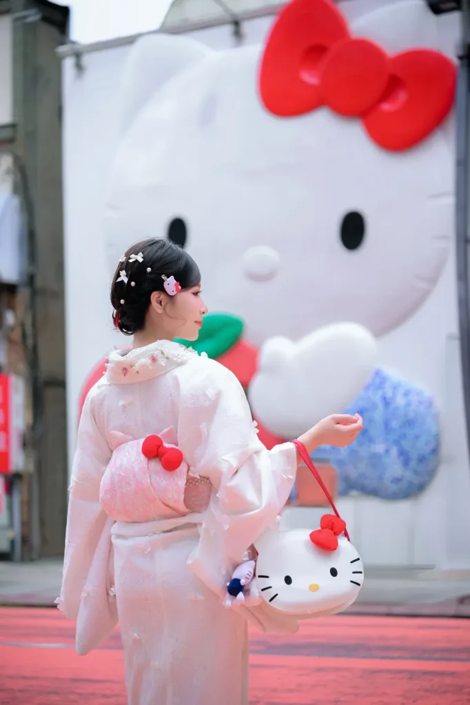 Back view of a girl in a pale pink kimono with a Hello Kitty handbag in front of a large Hello Kitty shop mural in Asakusa, Tokyo