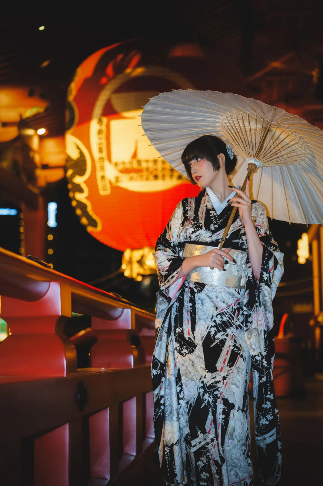 Guest in a black kimono holding a parasol, a huge red paper lantern glowing behind her