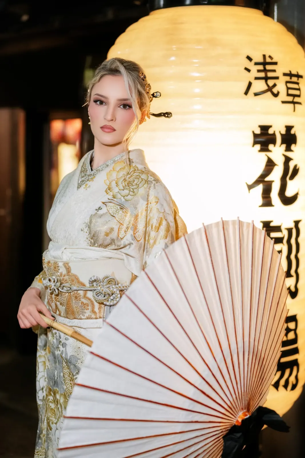 Guest in a gold kimono beside a large illuminated lantern on Hanayashiki Street at night