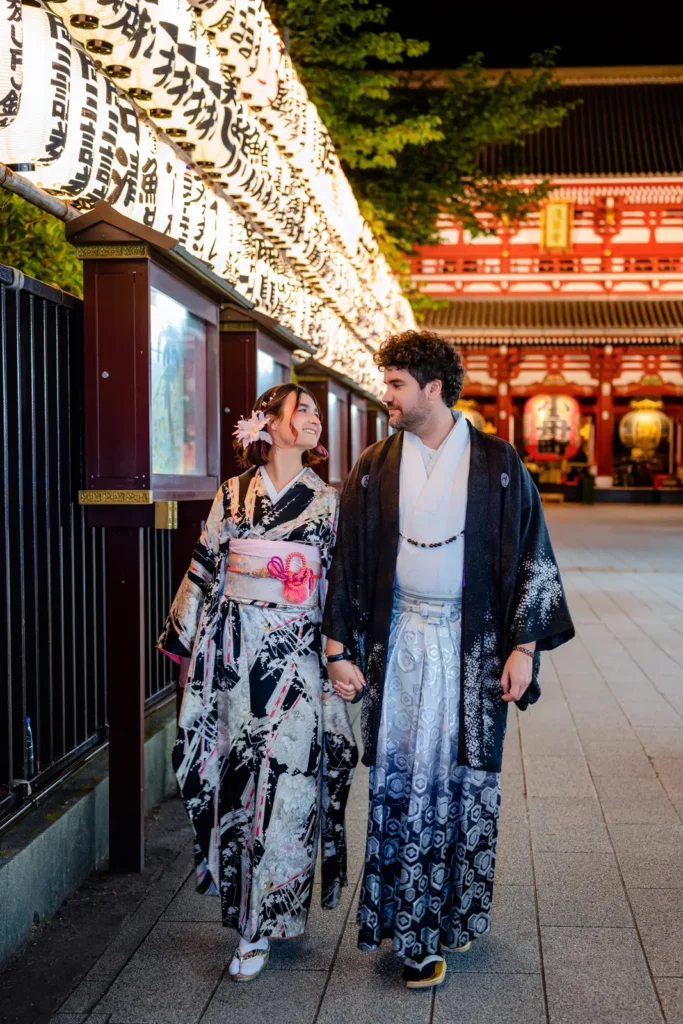 Couple in kimono holding hands and walking past a row of glowing paper lanterns at Sensoji Temple at night in Asakusa, Tokyo