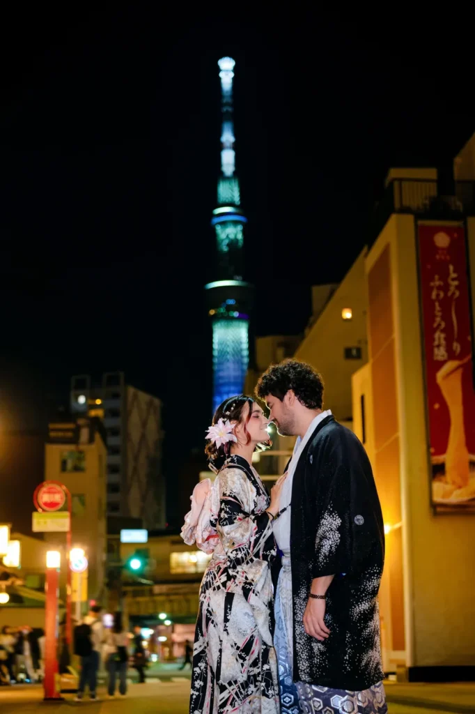 Couple in kimono standing face to face on an Asakusa street at night with the illuminated Tokyo Skytree behind them