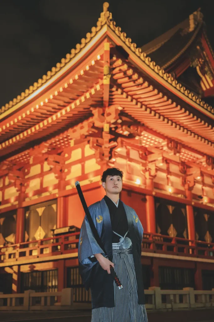 Guest in a grey kimono below the floodlit curved eaves of the Sensoji Main Hall at night