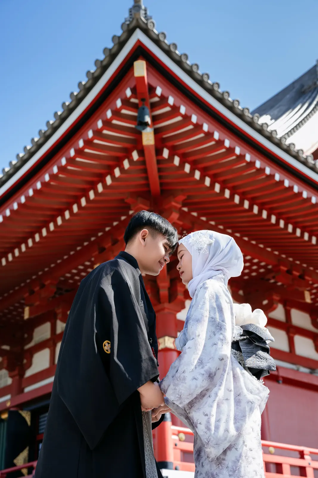 Couple in kimono, one in a white hijab, beneath the lit red roof of Sensoji at night