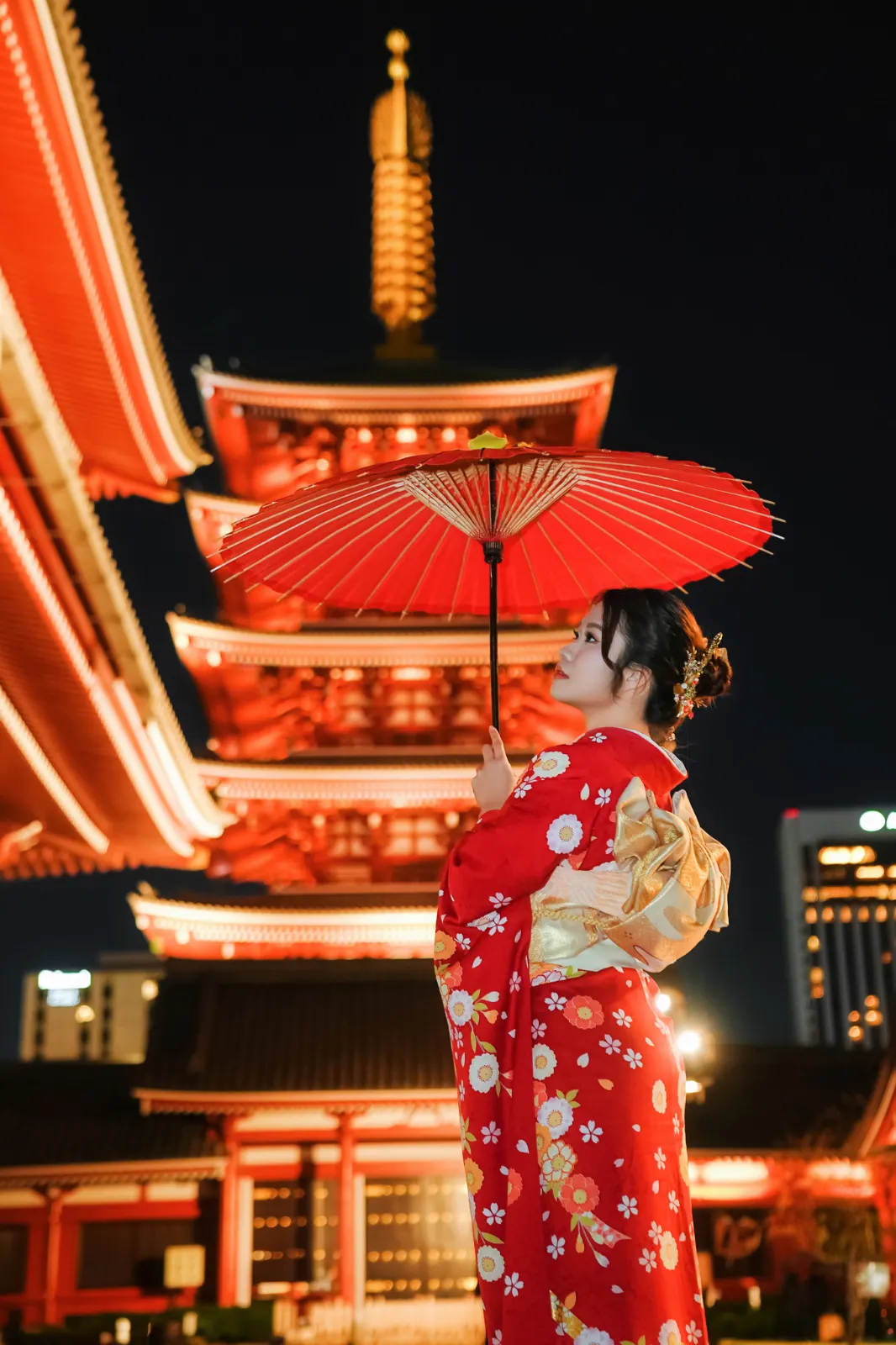 Guest in a red kimono with a red parasol, the five-storied pagoda lit gold against a black sky