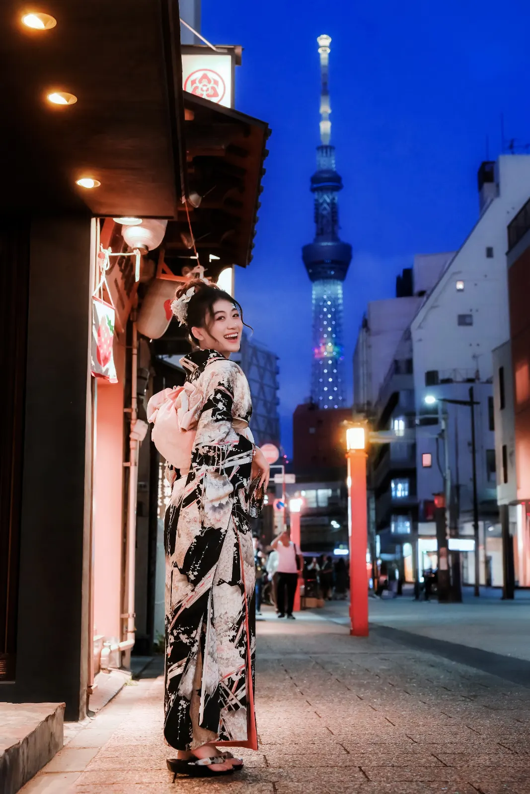 Guest in kimono on an Asakusa street at night with Tokyo Skytree lit blue behind