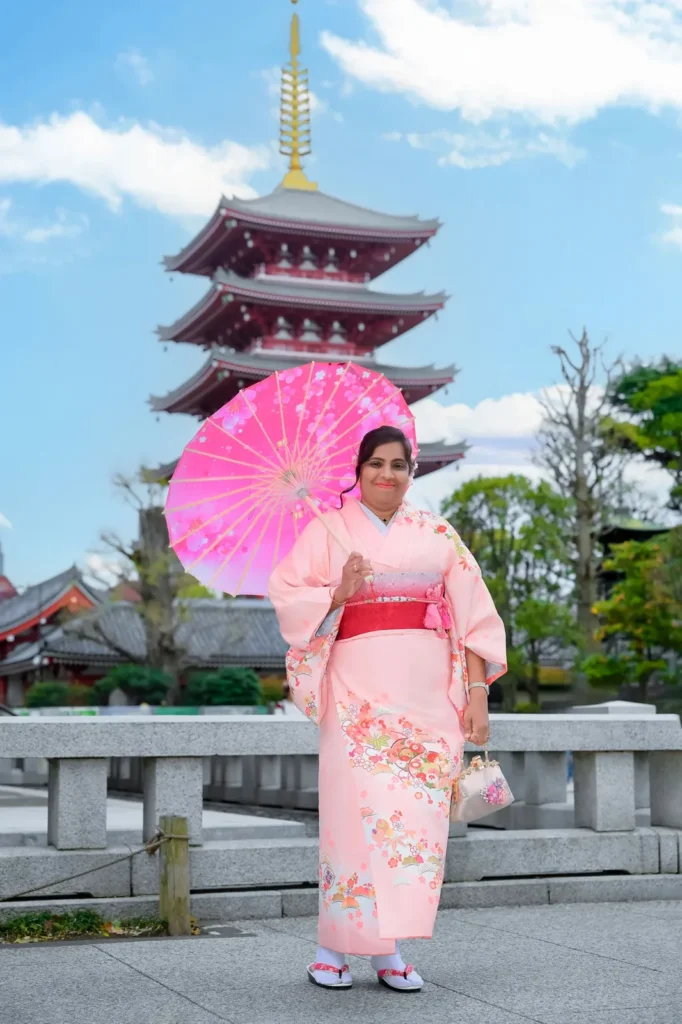 Soft pink plus size kimono with a sakura wagasa parasol beside the Sensoji five-story pagoda
