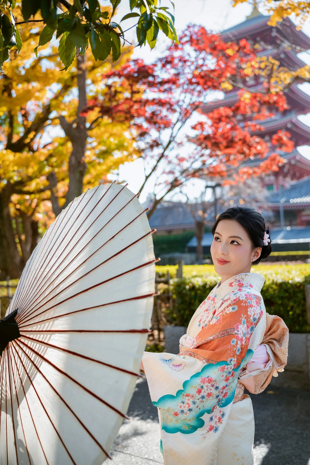 Woman in kimono with a paper umbrella under red maple leaves near the Five-Storied Pagoda at Sensoji
