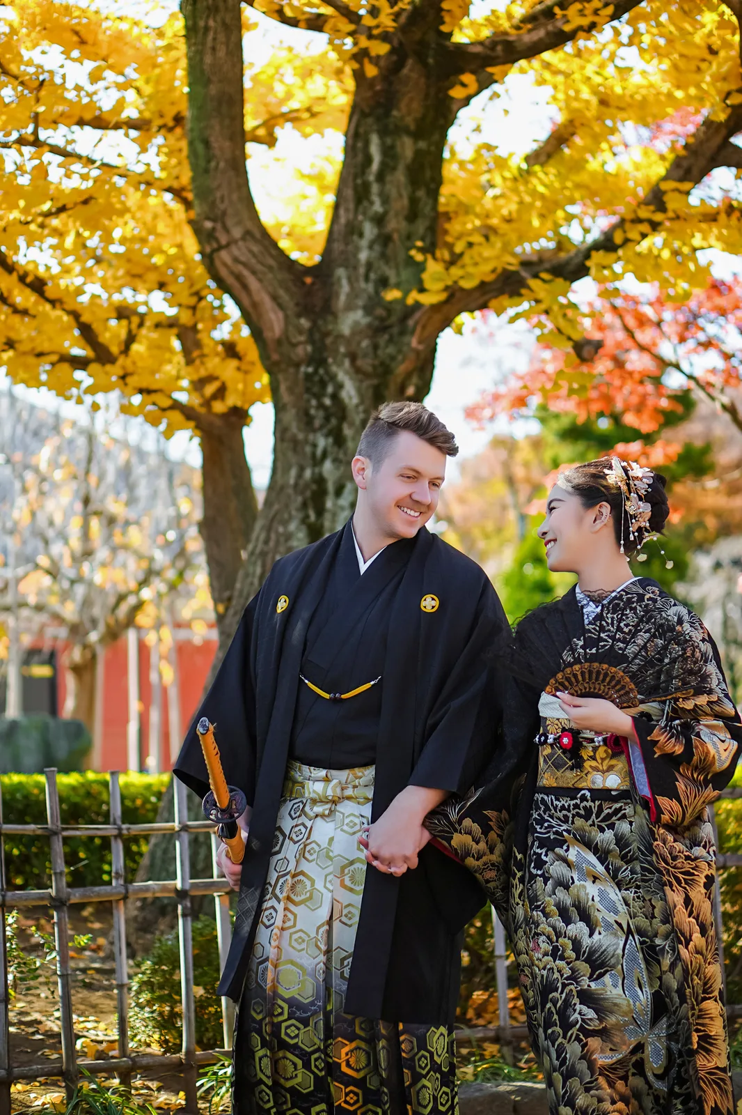 Couple in black kimono and hakama under golden ginkgo and red maple at Sensoji, Asakusa
