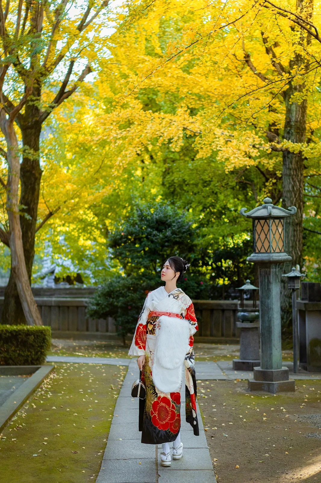Woman in white and red furisode on a stone path under golden ginkgo trees at Matsuchiyama Shoden, Asakusa