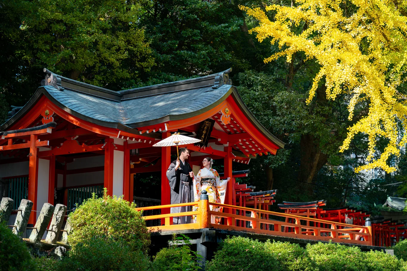 Red shrine hall above a pond surrounded by autumn leaves at Nezu Shrine, couple in kimono