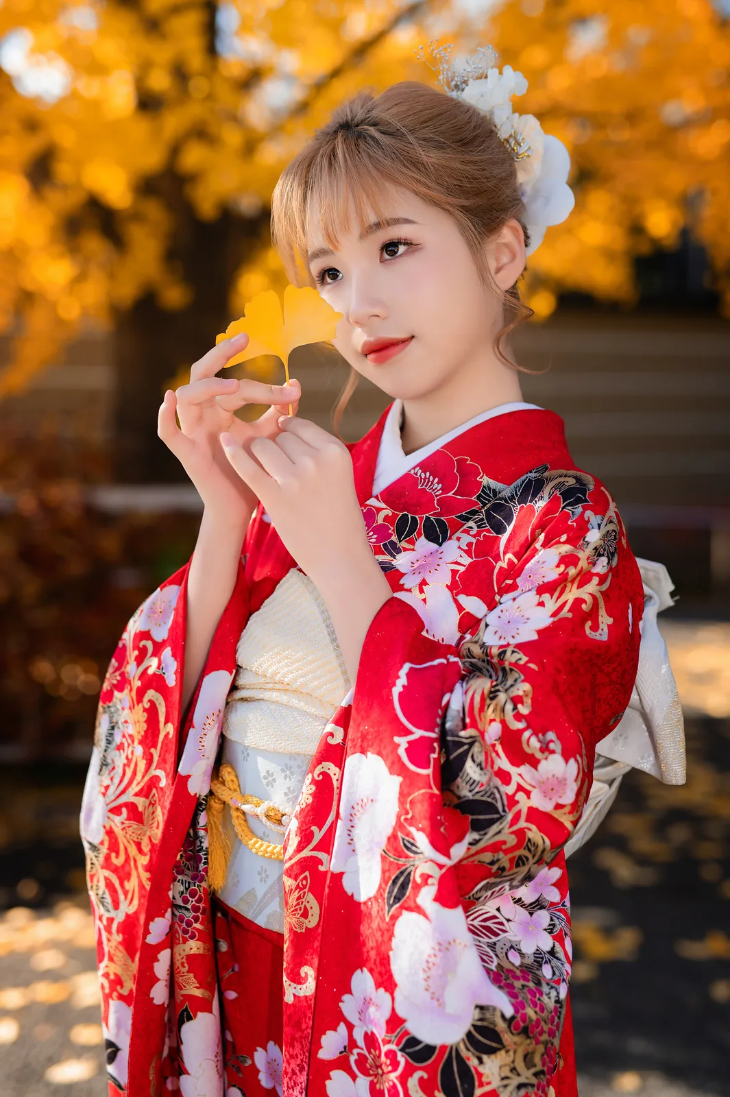 Close-up of a woman in red kimono holding a yellow ginkgo leaf in Ueno Park