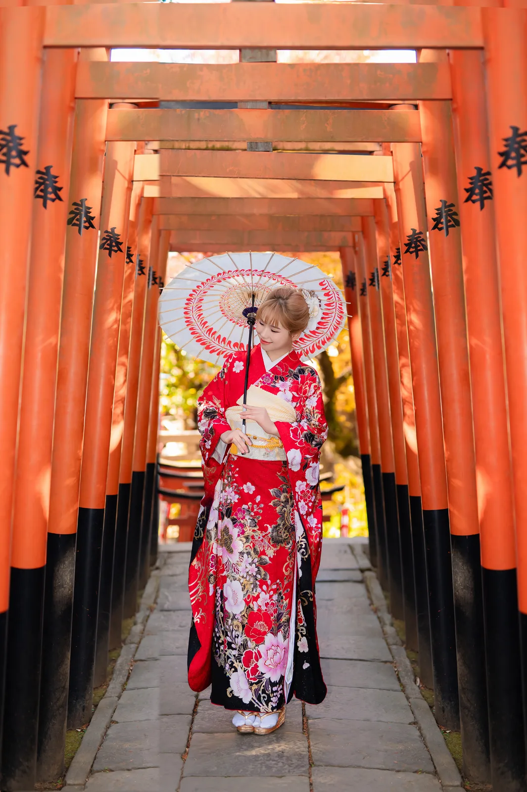 Woman in red kimono with a paper umbrella inside a tunnel of red torii gates in Ueno Park