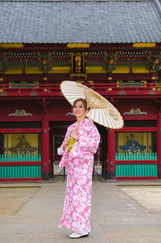 Woman in a pink floral basic kimono holding a Japanese paper umbrella in front of a shrine – basic kimono rental in Asakusa at Kimono Rental Ann
