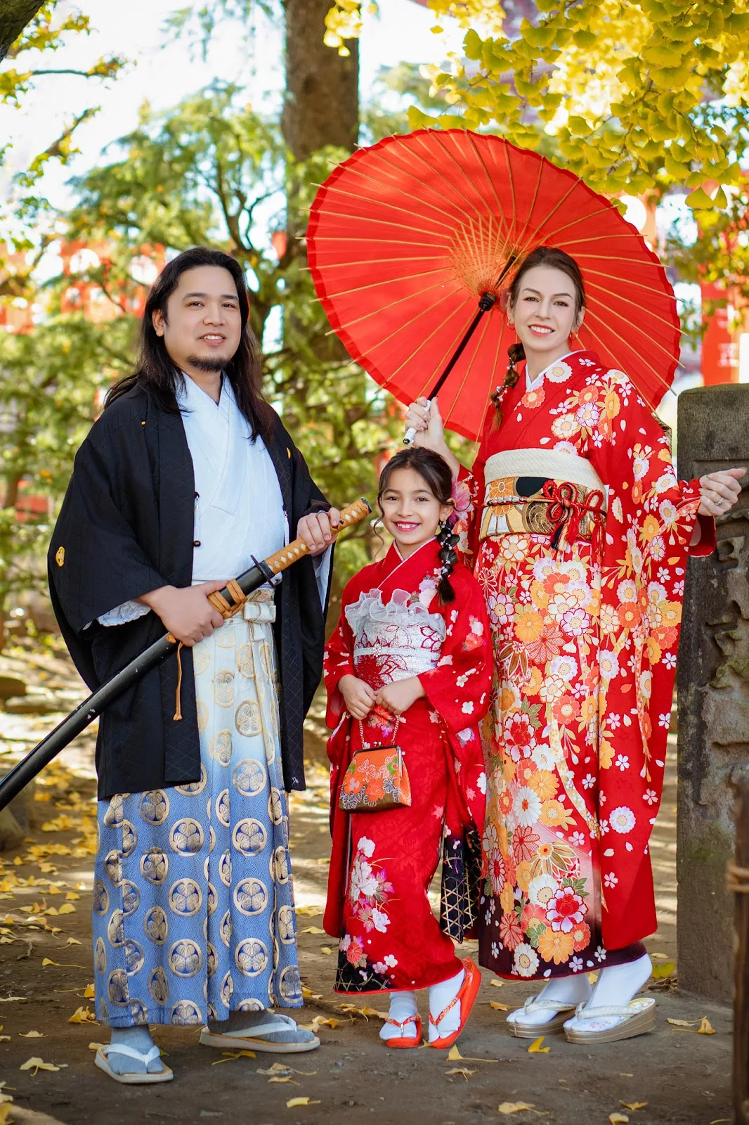 Father, mother and daughter in red kimono with a red paper umbrella under autumn trees in Asakusa