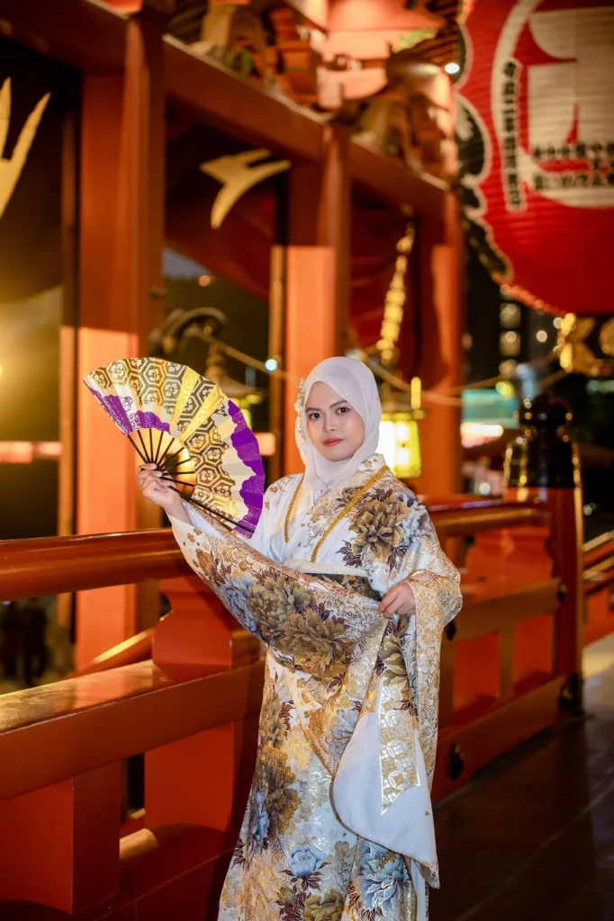 Guest in a white hijab and white and gold furisode holding a gold folding fan at Sensoji Temple at night, Asakusa