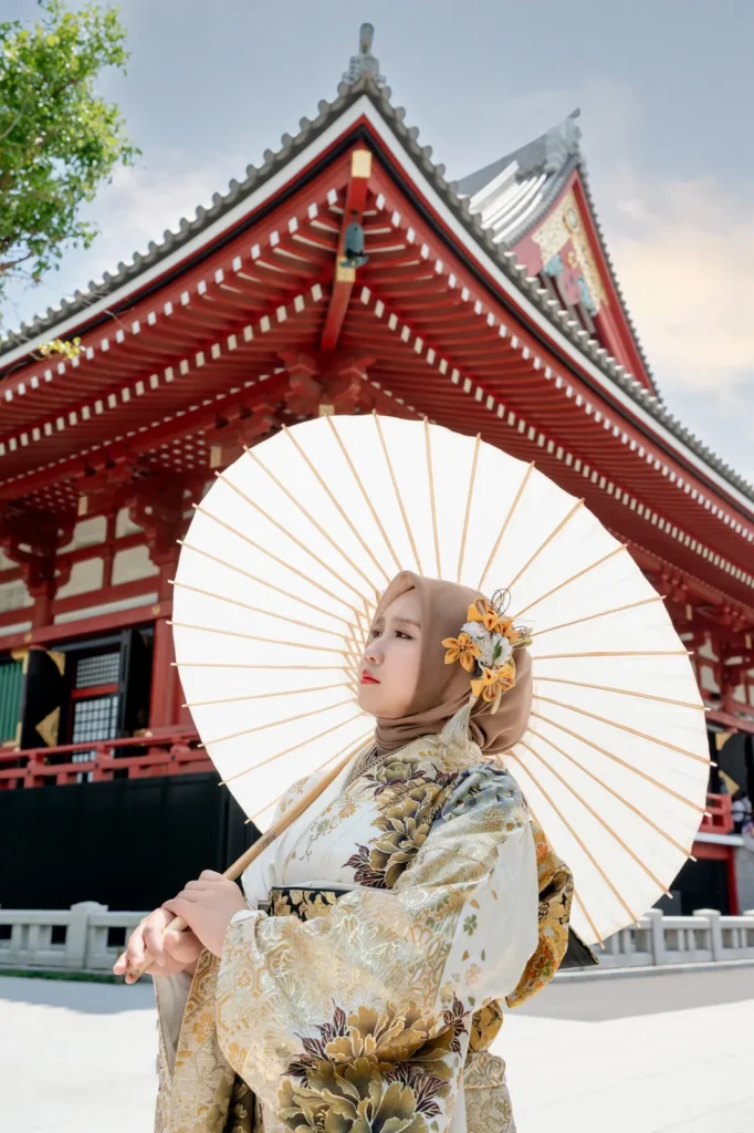Orange flower ornament pinned on a beige hijab, worn with a gold kimono and white paper parasol at Sensoji