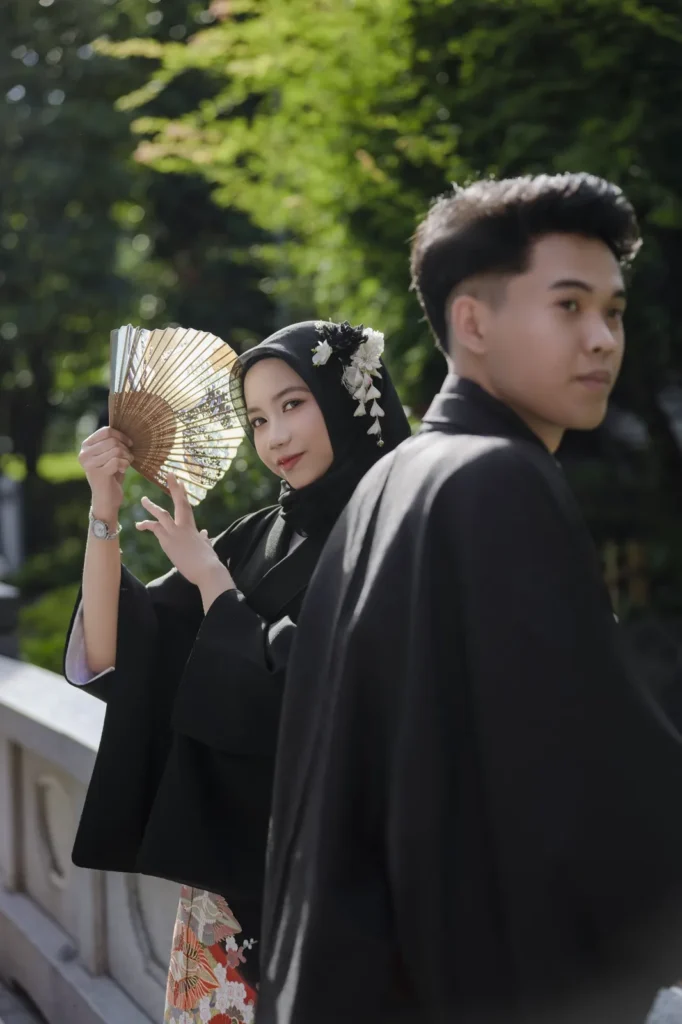 White kanzashi hair ornaments on a black hijab as a contrast accent, with a black kimono and folding fan