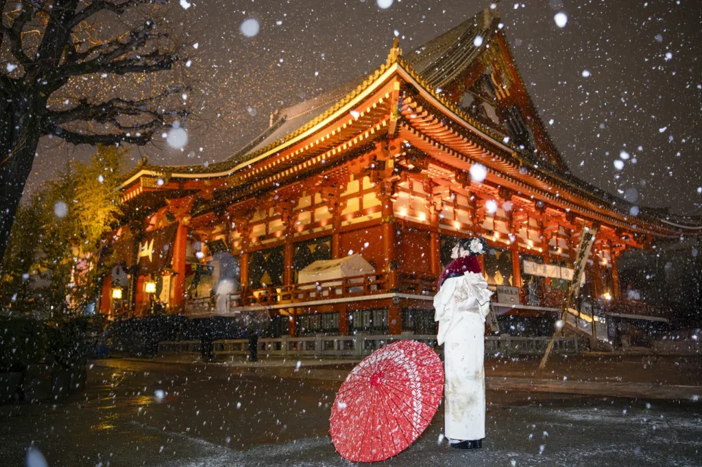 Red paper parasol and white kimono in the snow in front of Sensoji main hall on a winter night in Tokyo