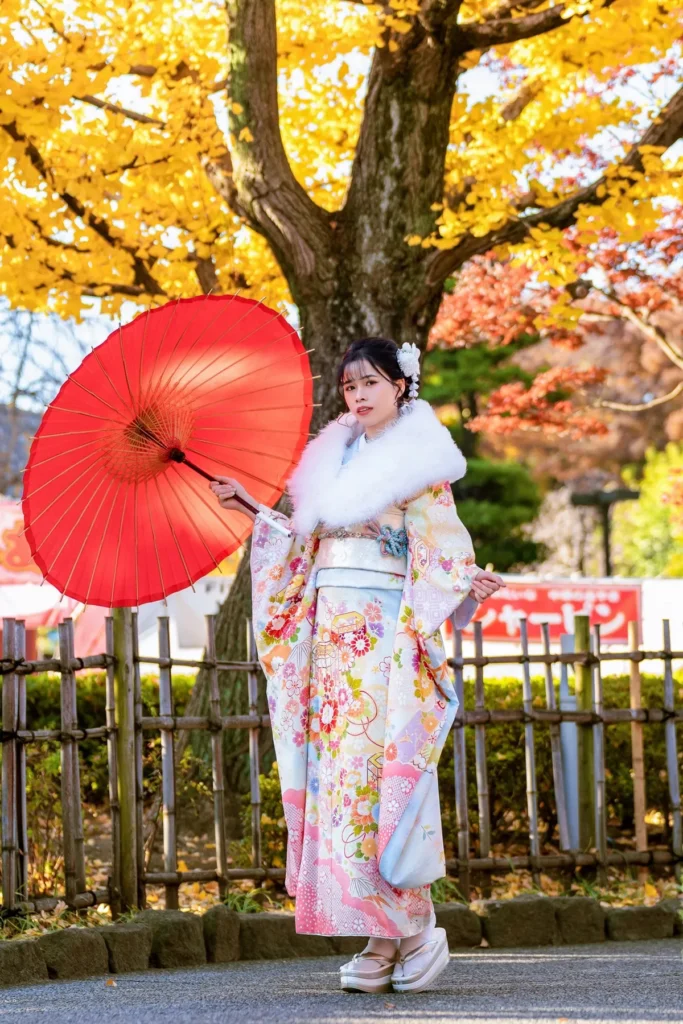Pastel floral furisode, white fur shawl and red parasol under yellow ginkgo leaves in early winter, Asakusa