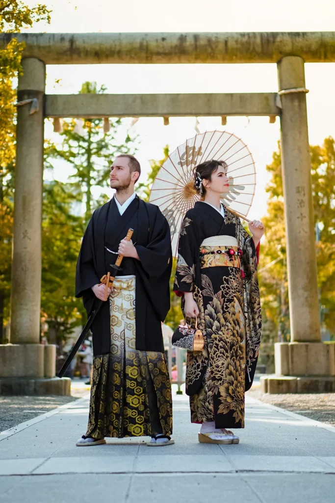 Couple in black kimono and hakama with a paper parasol under the stone torii of Asakusa Shrine