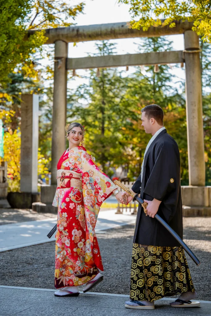 Couple in a red furisode and black montsuki hakama under the stone torii of Asakusa Shrine