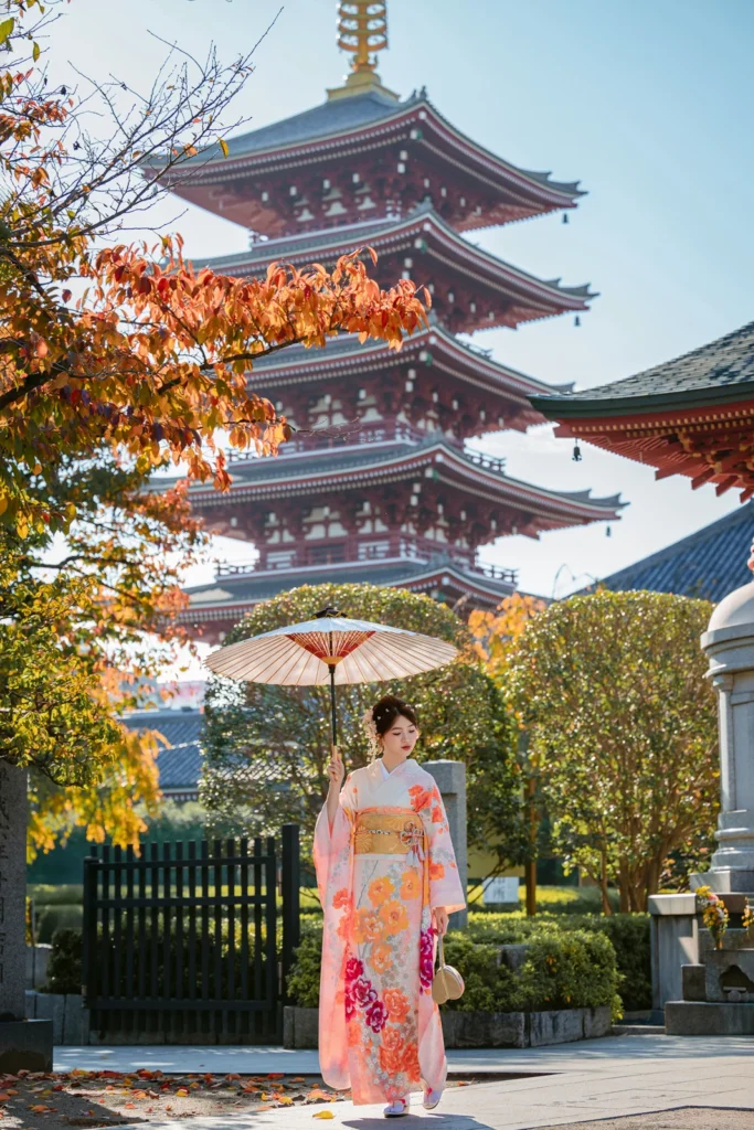 Guest in a pastel floral kimono with a parasol at Awashimado Hall, five-storied pagoda and autumn leaves behind