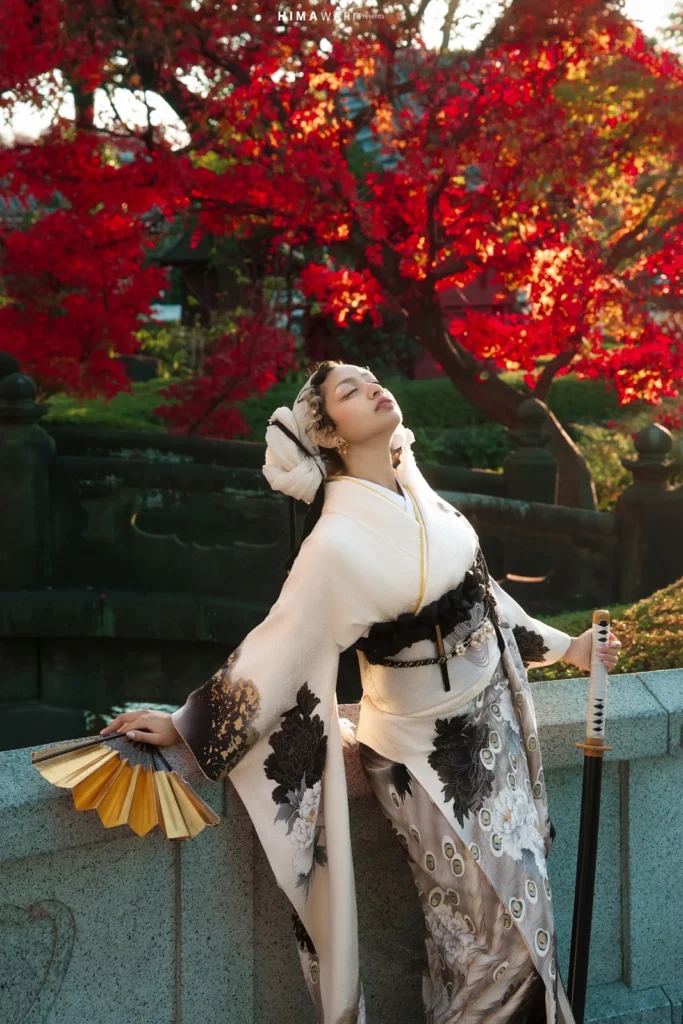 Woman in a white and black furisode with a gold fan under red autumn maple leaves at Rokkakudo, Sensoji
