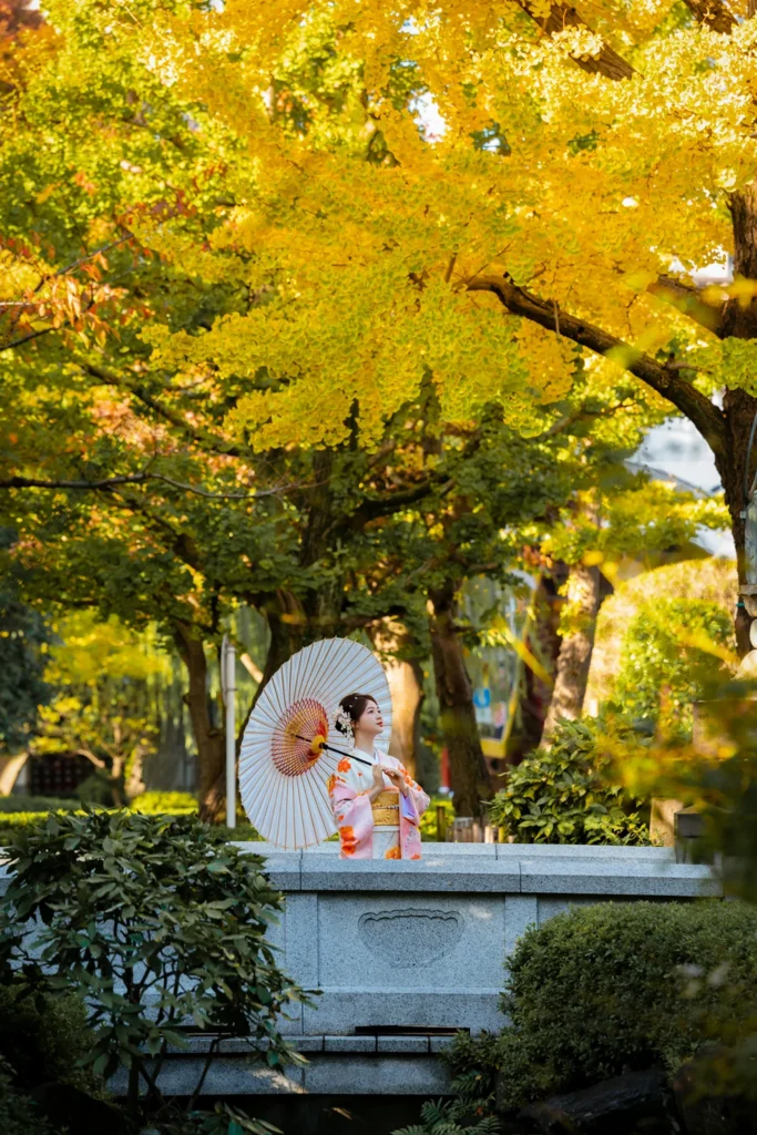 Guest with a paper parasol among yellow ginkgo trees at the six-sided Rokkakudo hall, Sensoji