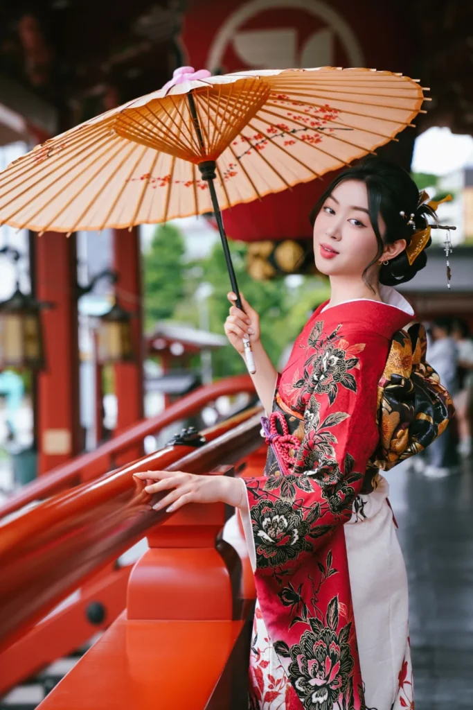 Woman in a red and black furisode with a paper parasol on the red steps of the Sensoji Main Hall