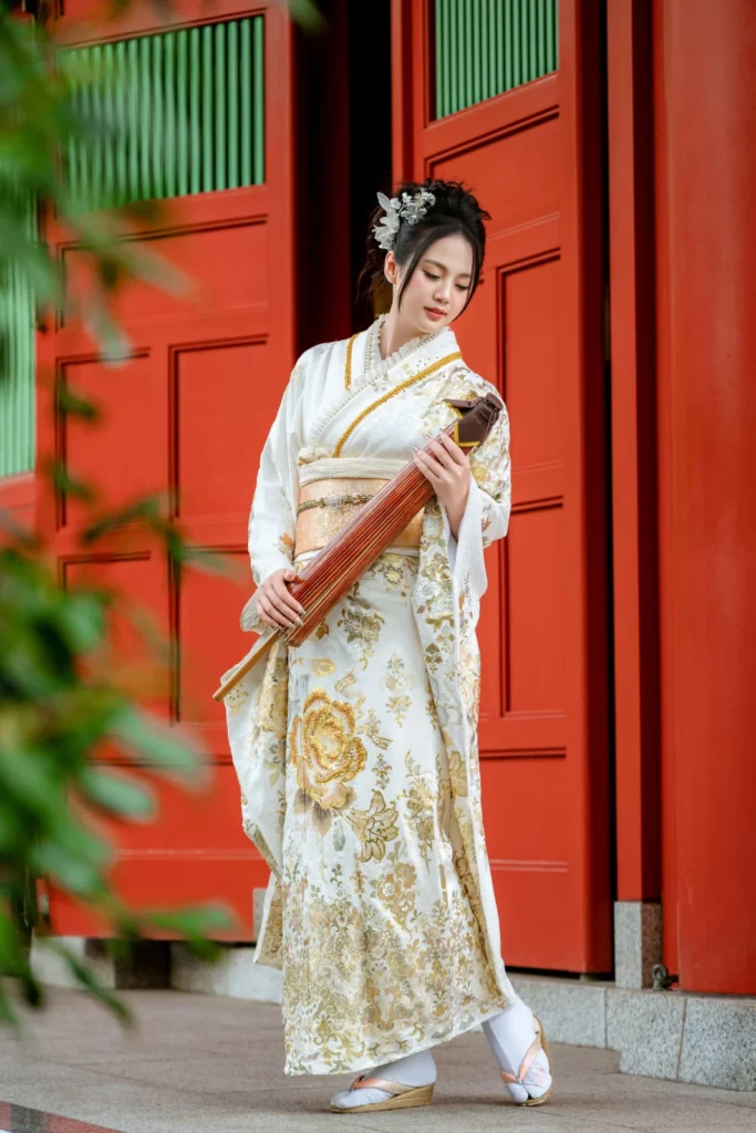 Woman in a white and gold furisode holding a parasol against the red doors of Yogodo Hall, Sensoji