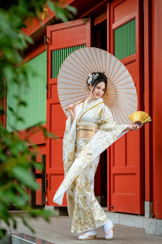 White and gold furisode with a paper parasol and gold fan at the red doors of Yogodo Hall, Asakusa
