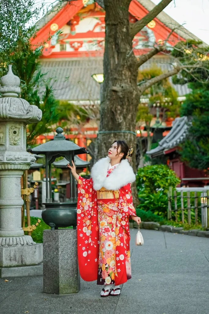 Red furisode and white fur shawl beside a stone lantern in the Sensoji Temple grounds in winter