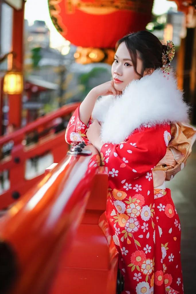 Kimono guest in a red furisode and white fur shawl leaning on a red railing in Asakusa, Tokyo