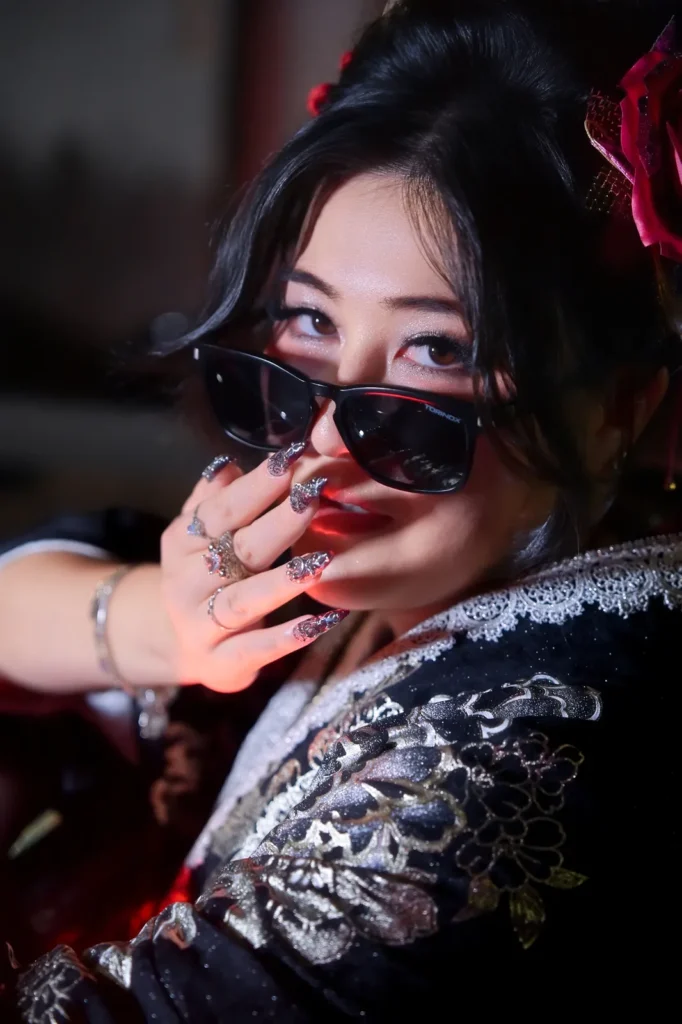 Close-up of a woman in a black and silver kimono lowering her sunglasses, with a red rose hair ornament