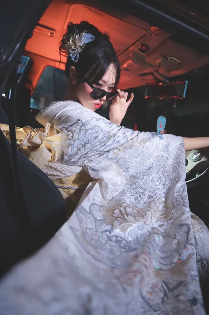 Woman in a white embroidered furisode wearing sunglasses in the driver seat of a JDM car