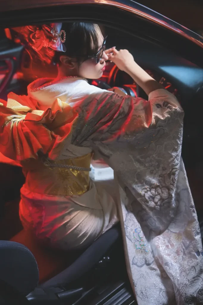 Woman in a red and white kimono wearing sunglasses inside a car lit in red