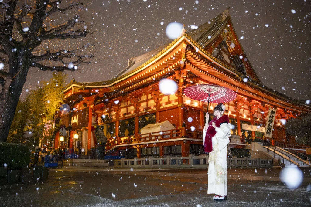Guest in a white kimono with a red parasol in falling snow at Sensoji Temple main hall, Asakusa, at night
